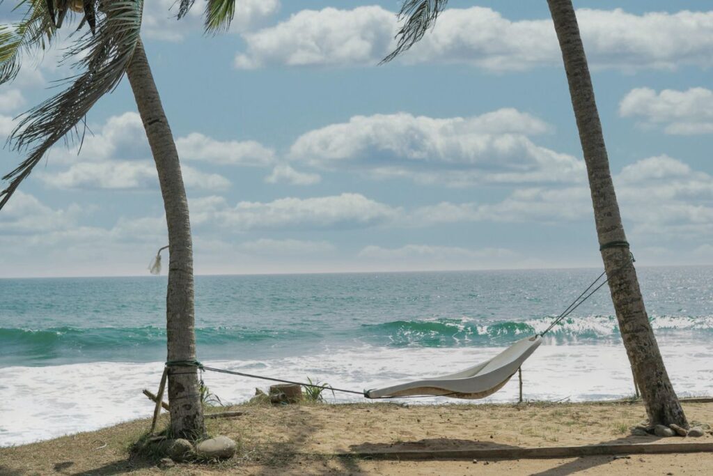 Hängematte zwischen zwei Palmen am Strand, im Hintergrund das Meer